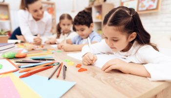 Children write in notebooks with a pen.